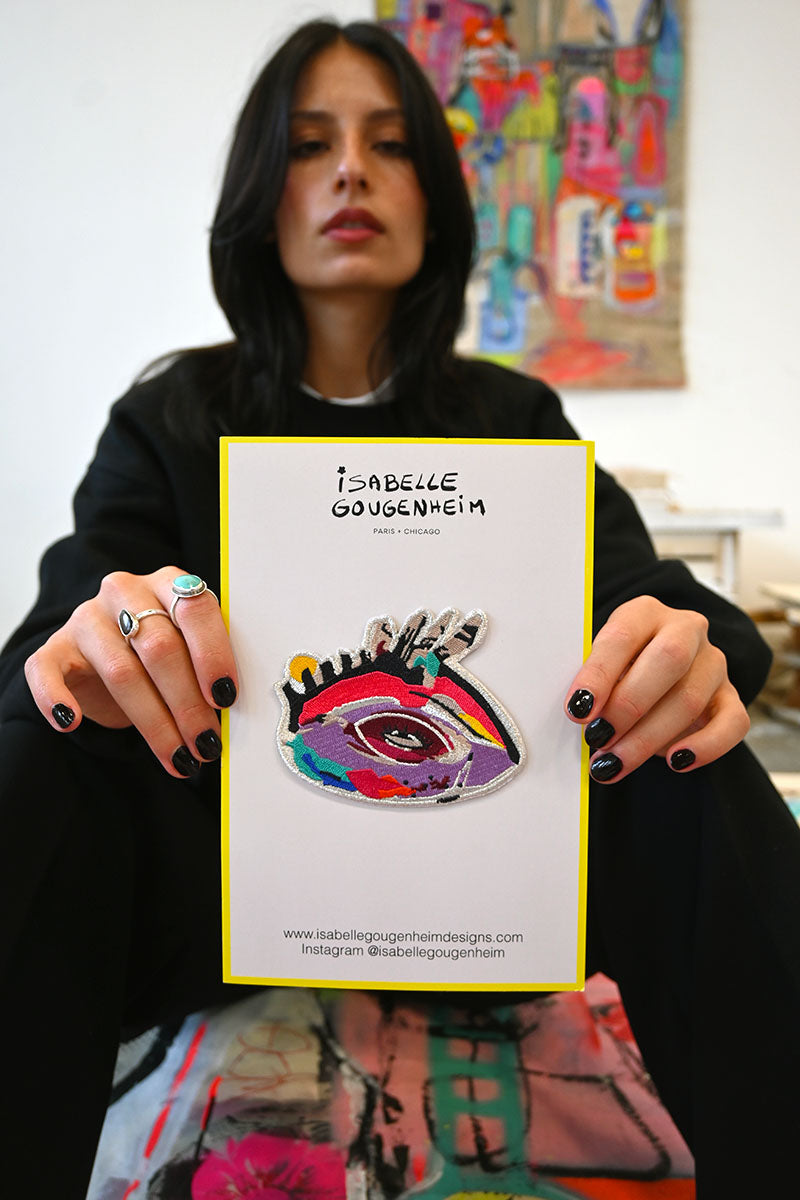 Person holding a card with a colorful eye design and 'Isabelle Dougenheim' branding.