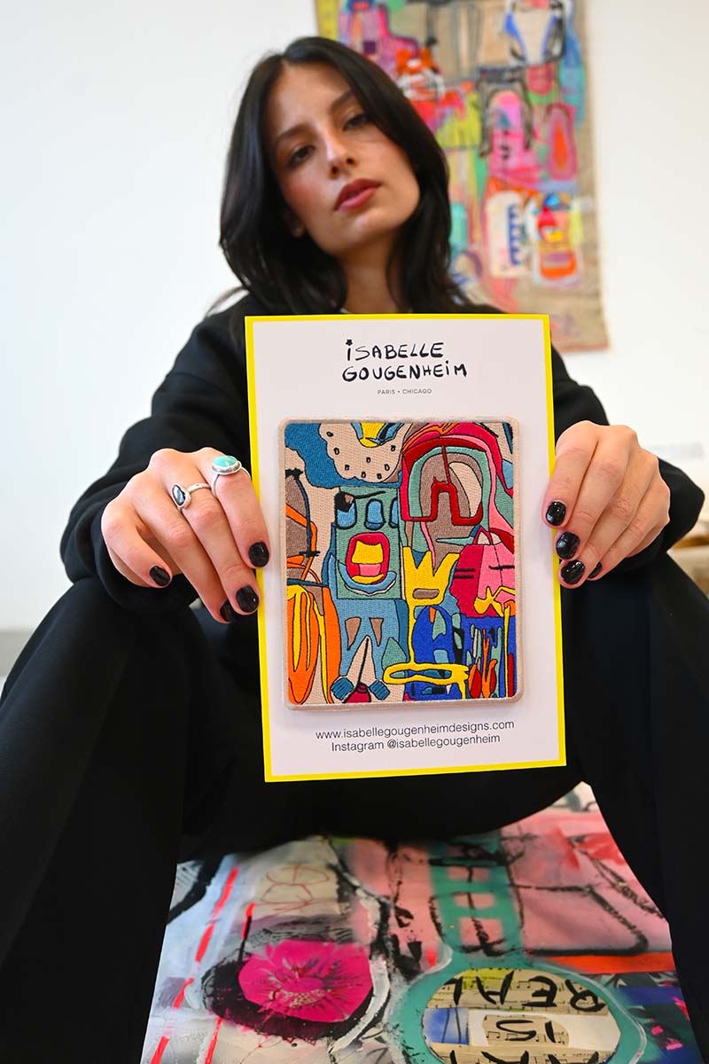 Woman holding a colorful card with 'Isabelle Gougenheim' branding in an artistic setting.