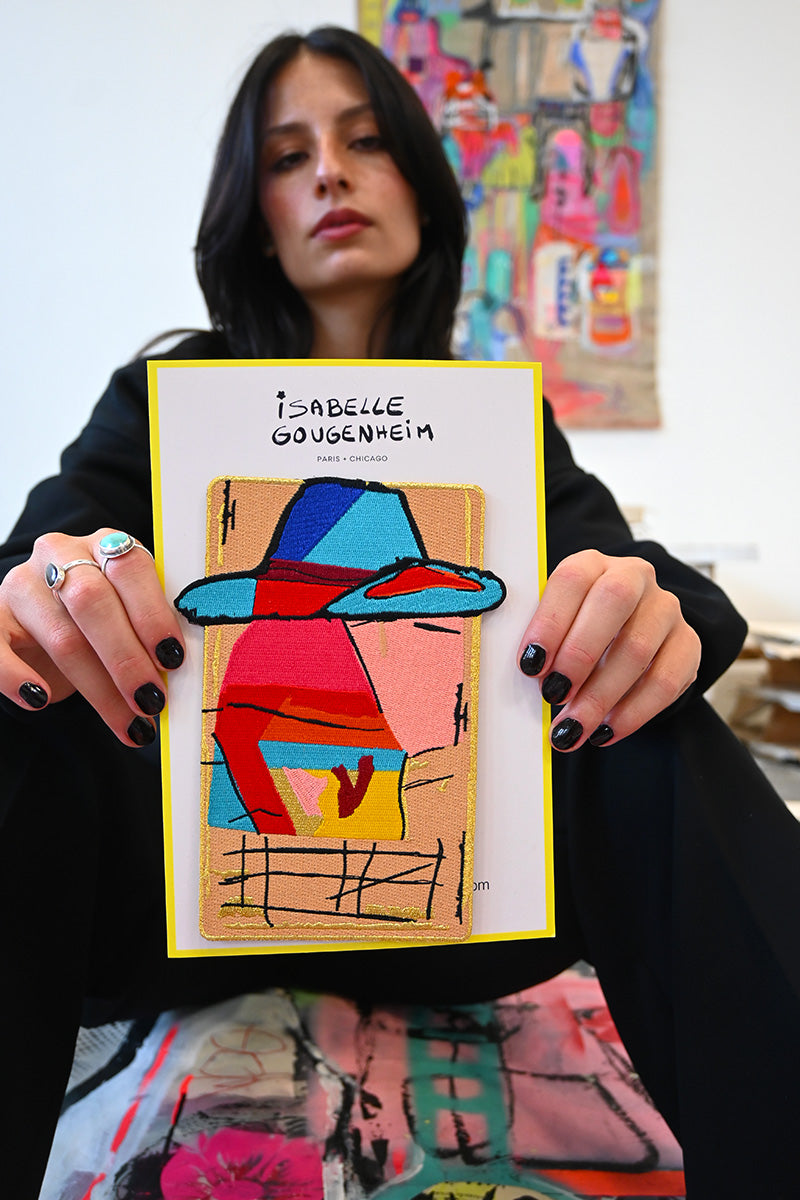 Woman holding a colorful abstract painting with 'Isabelle Gougenheim' on it, in an artistic setting.