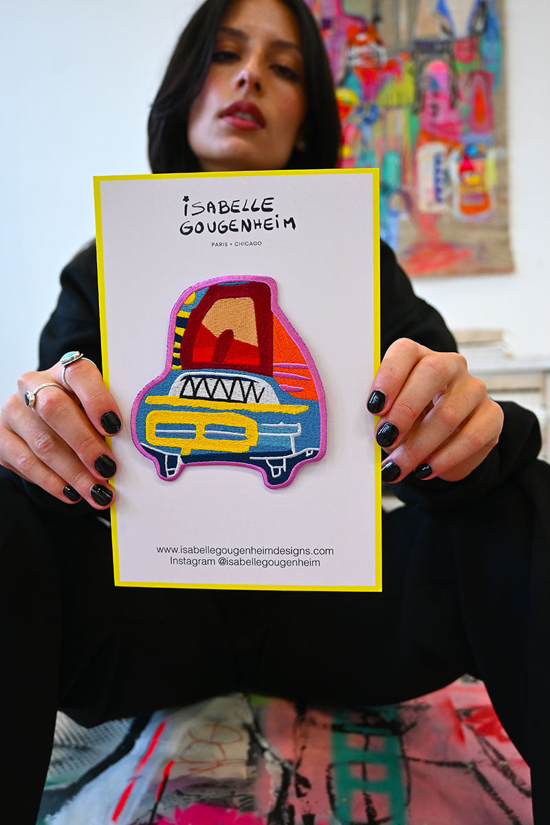 Person holding a colorful patch with 'Isabelle Gougenheim' branding against a vibrant background.