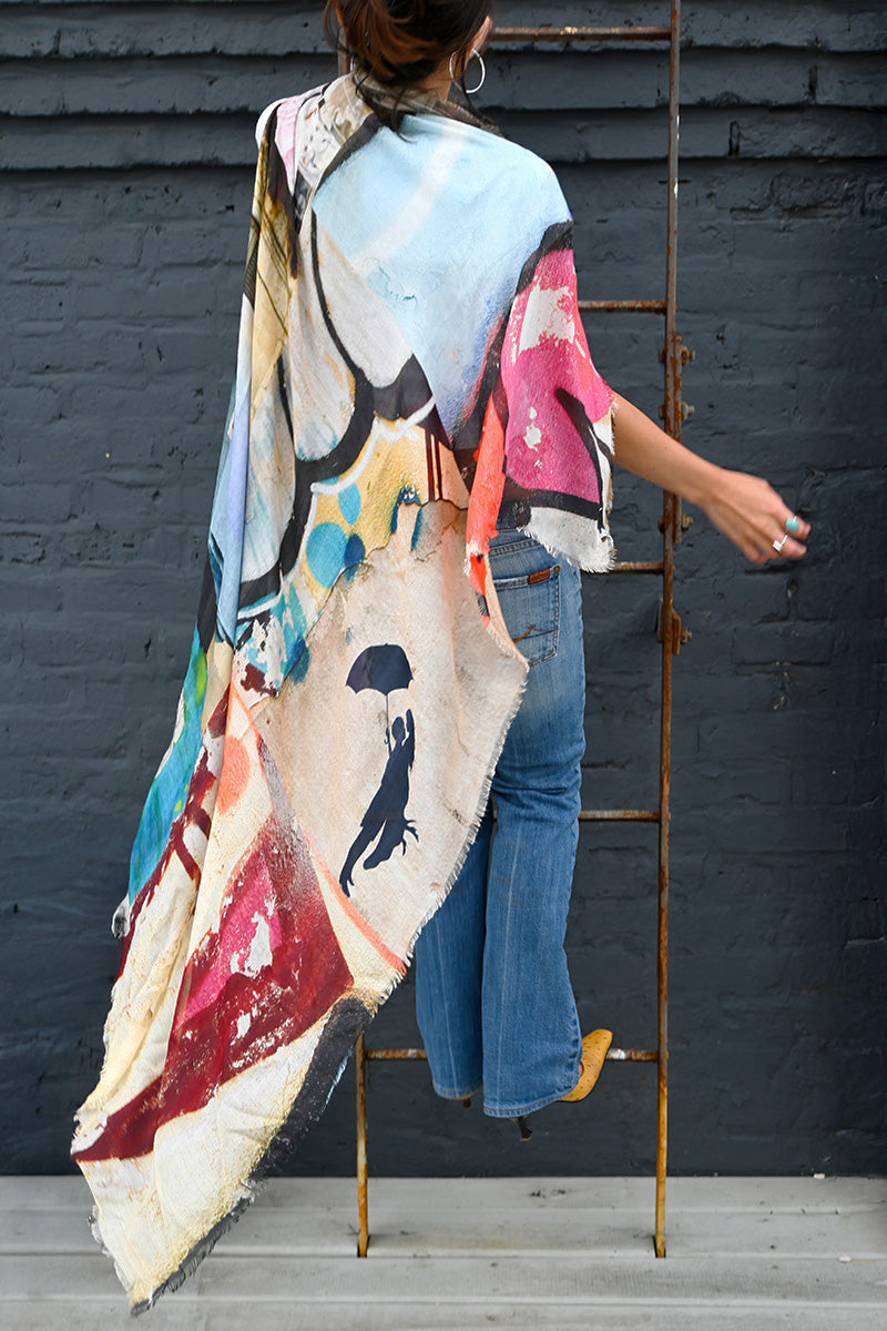 Model wearing the Moments Silk Scarf, featuring vibrant blue, pink, red and cream abstract artwork with fringed edges.