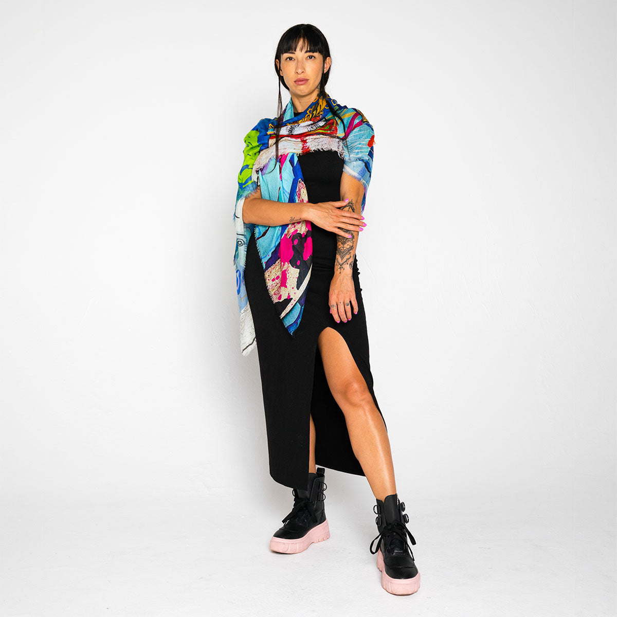 Person wearing a colorful scarf, black dress, and high-top sneakers on a white background